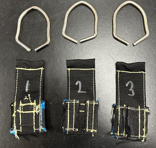 Three Ballistic Kevlar D-ring specimens after tensile testing at NC State: each steel D-ring has opened at its weld while the Kevlar-stitched webbing is intact